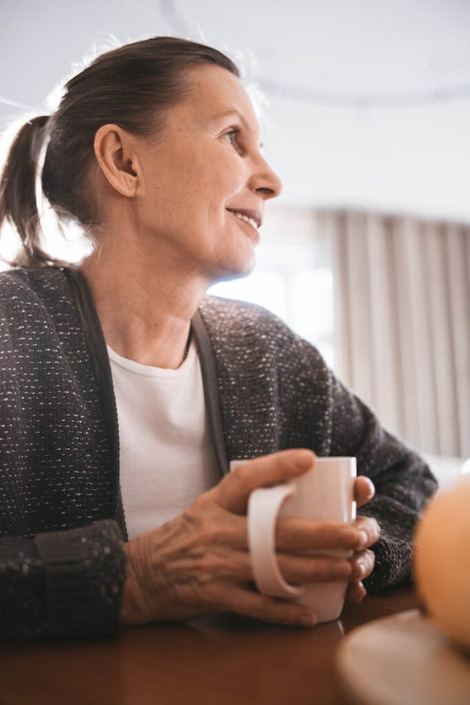 Senior woman holding a mug steadily, smiling and enjoying a warm drink indoors